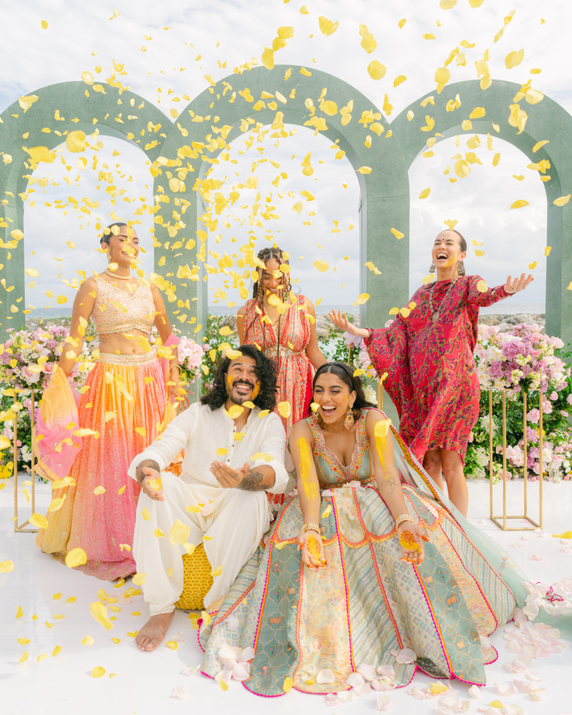 Joyful Haldi ceremony at a destination wedding, with family and friends celebrating as yellow flower petals fall.