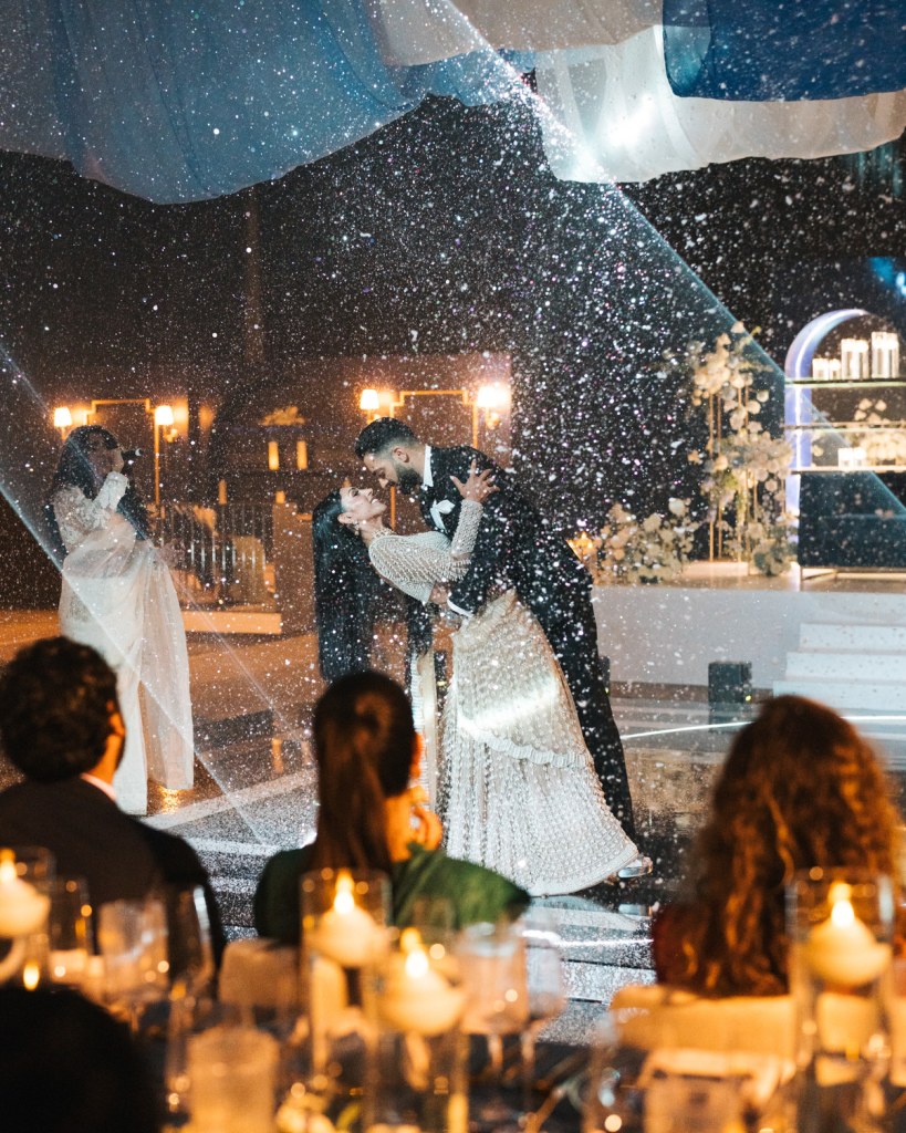Couple sharing their first dance at an outdoor destination wedding reception with sparkling lights and guests watching.