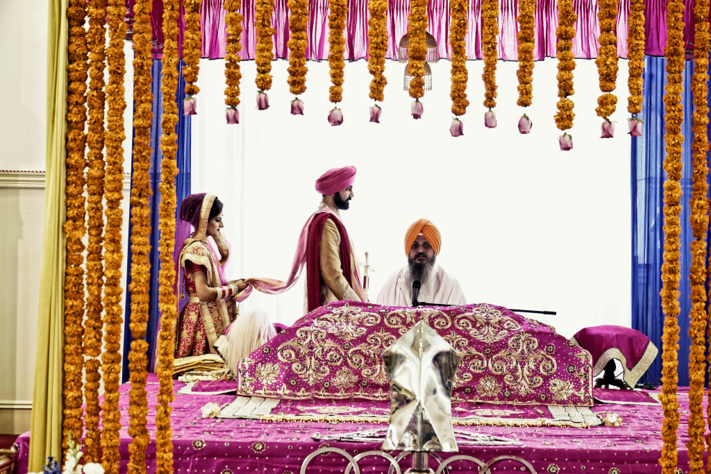 Granthi leading an Anand Karaj ceremony as the couple participates before the Guru Granth Sahib, following traditional Sikh wedding rituals.